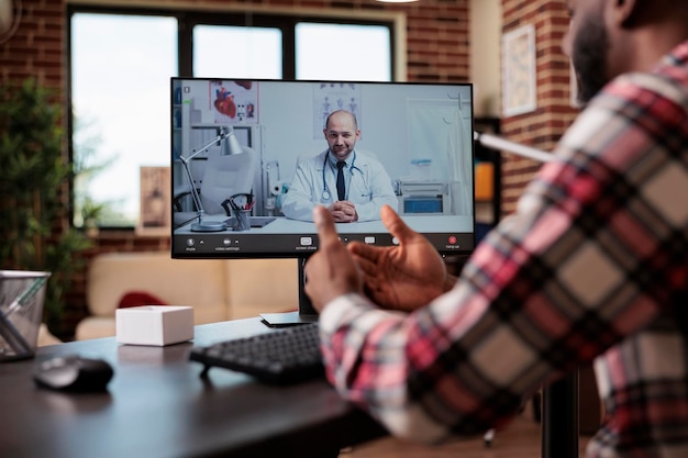Jeune homme parlant à un médecin lors d'une conférence de télémédecine par appel vidéo sur une connexion internet. Rencontre avec un médecin en vidéoconférence télésanté en ligne sur ordinateur, chat ou téléconférence à distance.