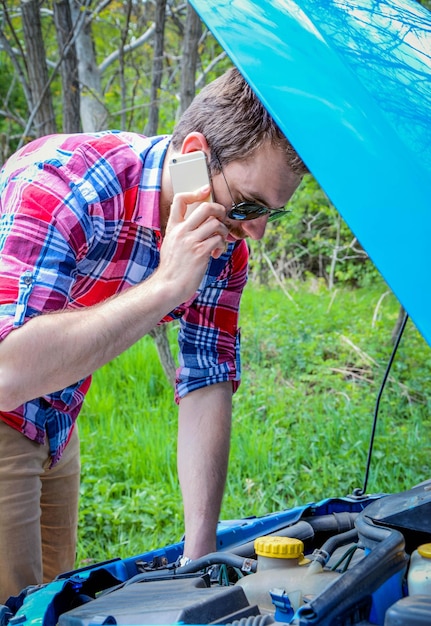 Photo un jeune homme parle au téléphone portable tout en vérifiant le moteur de la voiture.