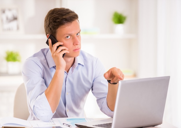 Jeune homme parle par téléphone tout en travaillant avec un ordinateur portable.