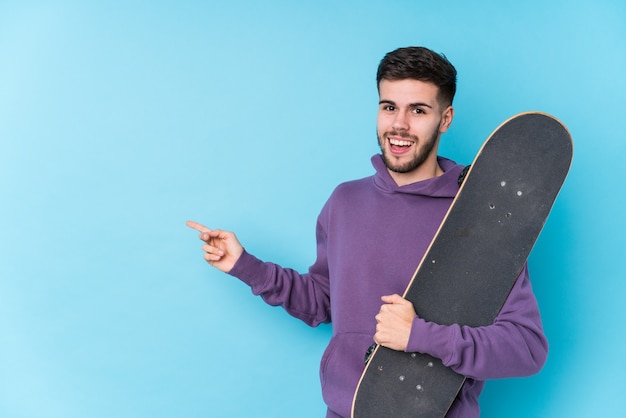 Jeune homme de patineur caucasien isolé souriant et pointant de côté, montrant quelque chose à l'espace vide.