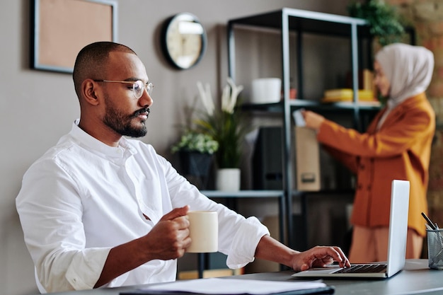 Jeune homme PDG en chemise blanche regardant un écran d'ordinateur portable contre une collègue