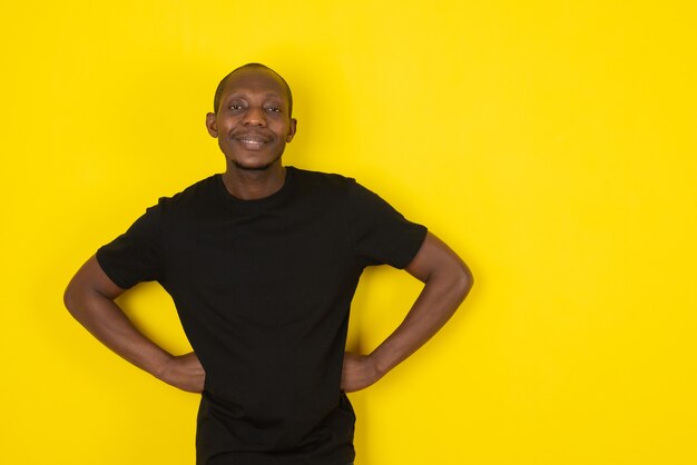 Photo jeune homme à la peau foncée debout et posant sur un mur jaune