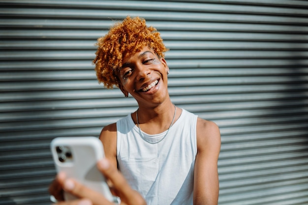 Photo jeune homme à la peau noire posant dans la rue et prenant un selfie dans l'arrière-plan de la ville homme souriant et