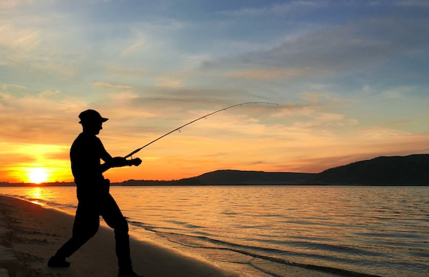 Jeune homme pêchant sur un lac au coucher du soleil