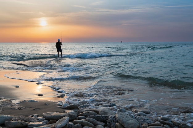 Jeune homme pêchant seul au bord de la mer à marée basse au coucher du soleil.