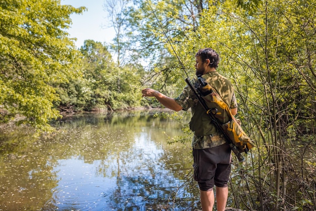 Jeune homme un pêcheur d'eau douce tenant une canne à pêche avec une bobine de filature se prépare à attraper un