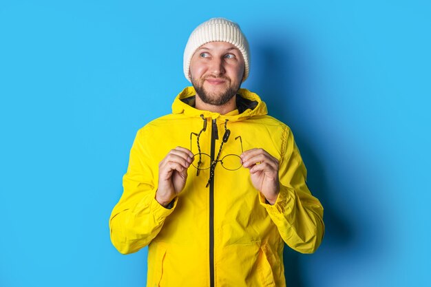 Jeune homme pensif tenant des lunettes dans une veste jaune sur fond bleu.