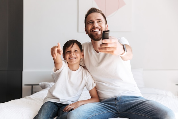 Jeune homme père papa s'amusant avec son fils à regarder la télévision tenant la télécommande.