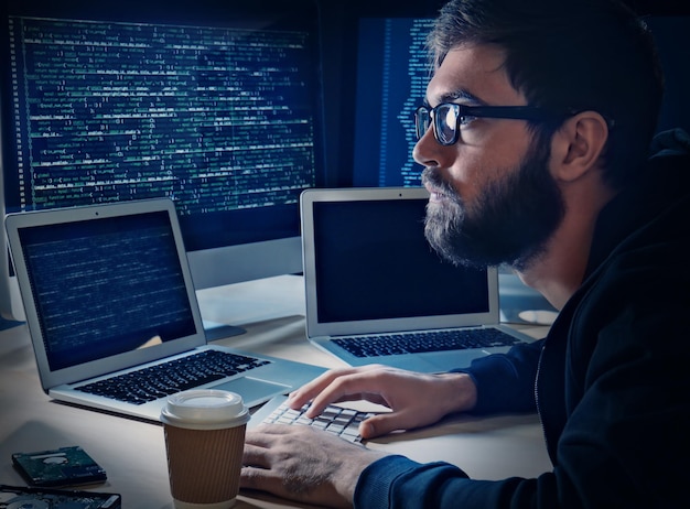 Jeune homme piratant un serveur dans une pièce sombre