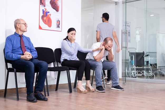 Jeune homme pleurant tenant la main de sa femme dans le couloir de l'hôpital après des nouvelles défavorables d'un spécialiste médical