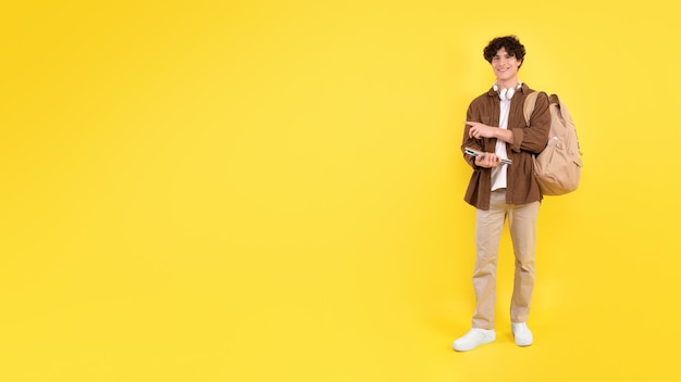 Jeune homme pointant vers l'espace libre tenant des cahiers sur fond jaune