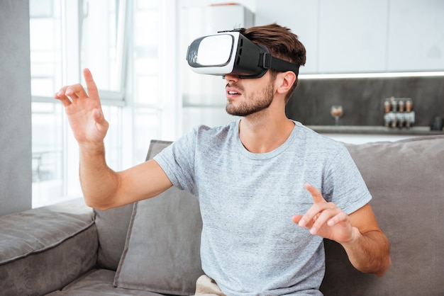 Jeune homme portant un appareil de réalité virtuelle alors qu'il était assis sur un canapé