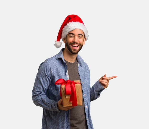 Jeune homme portant le bonnet de Noel pointant sur le côté avec le doigt
