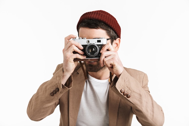 jeune homme portant un chapeau hipster se réjouissant tout en tenant et en photographiant sur le devant rétro isolé sur un mur blanc