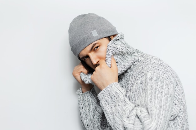 jeune homme portant chapeau et pull sur un mur blanc.