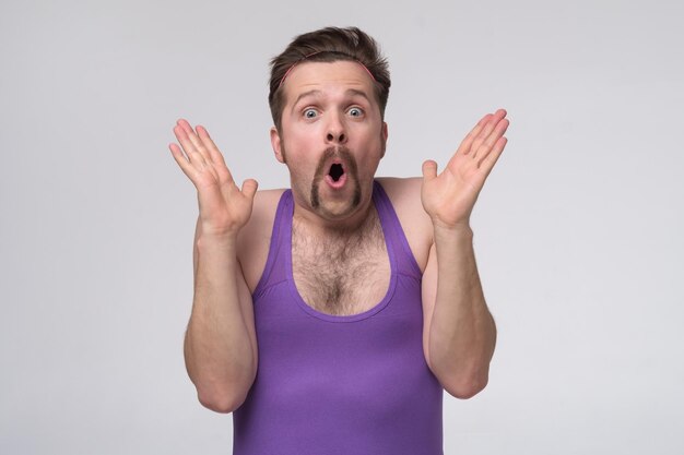 Jeune homme portant une chemise violette de sport choqué par une expression surprise et un visage excité