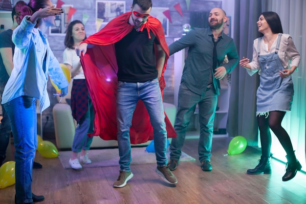 Jeune homme portant un costume de super-héros dans une pièce avec des ballons dansant avec ses amis.