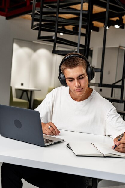 Photo un jeune homme portant des écouteurs alors qu'il étudie avec un ordinateur portable