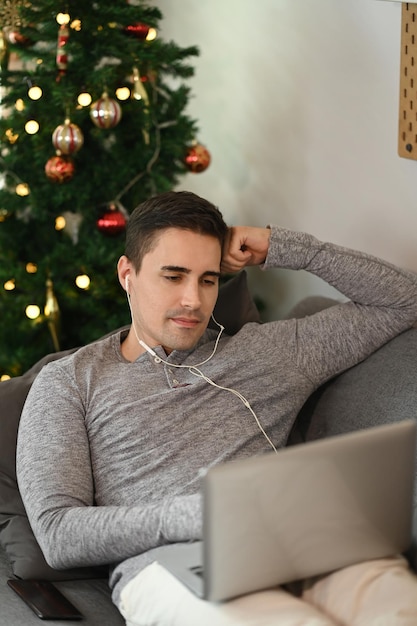 Jeune homme portant des écouteurs et naviguant sur Internet avec un ordinateur portable sur un canapé