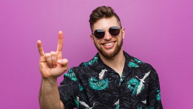 Jeune homme portant un look de vacances montrant un geste de cornes