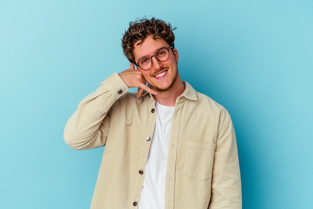 Jeune homme portant des lunettes isolé sur un mur bleu montrant un geste d'appel de téléphone mobile avec les doigts