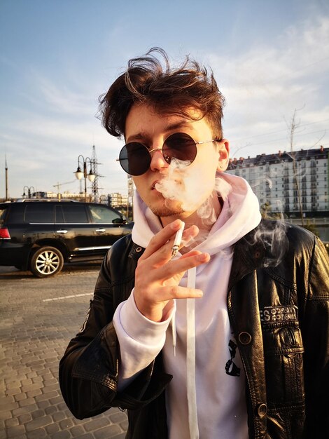 Photo un jeune homme portant des lunettes de soleil debout à côté de la voiture contre le ciel