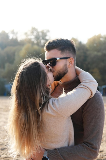 Un jeune homme portant des lunettes de soleil noires embrasse une fille par la taille et l'embrasse