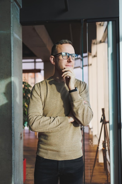 Un jeune homme portant des lunettes et des vêtements décontractés se tient dans un espace de travail moderne