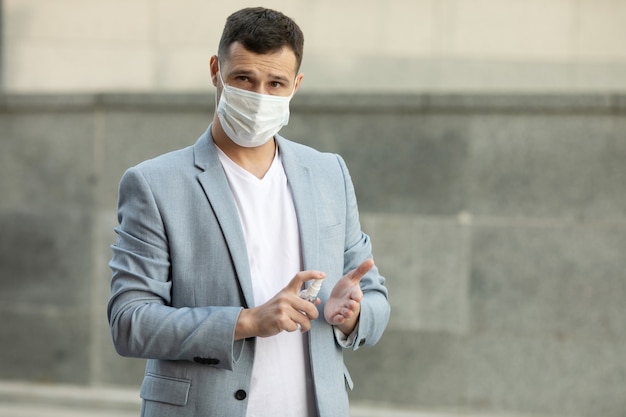 Jeune homme portant un masque médical à l'aide de gel désinfectant pour les mains marchant dans la ville