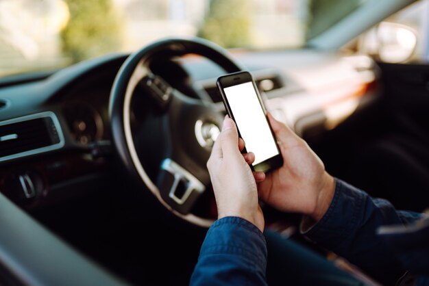 Jeune homme portant un masque médical stérile protecteur utilisant un téléphone au volant d'une voiture.