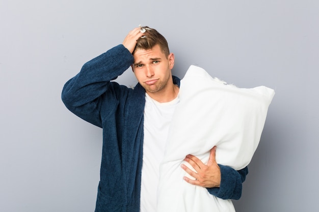 Jeune homme portant un pijama tenant un oreiller sous le choc, elle s'est souvenue d'une réunion importante.