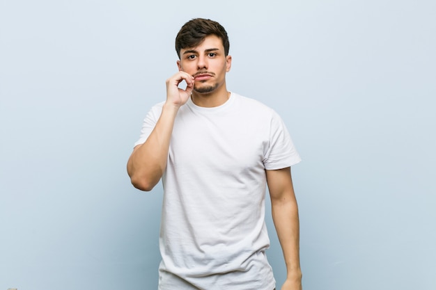 Jeune homme portant un t-shirt blanc avec les doigts sur les lèvres gardant un secret