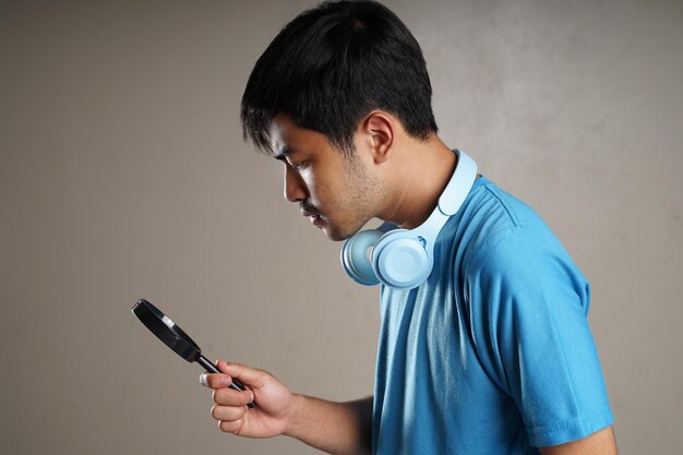 Un jeune homme portant un t-shirt bleu et des écouteurs tient sérieusement une loupe face vers le bas