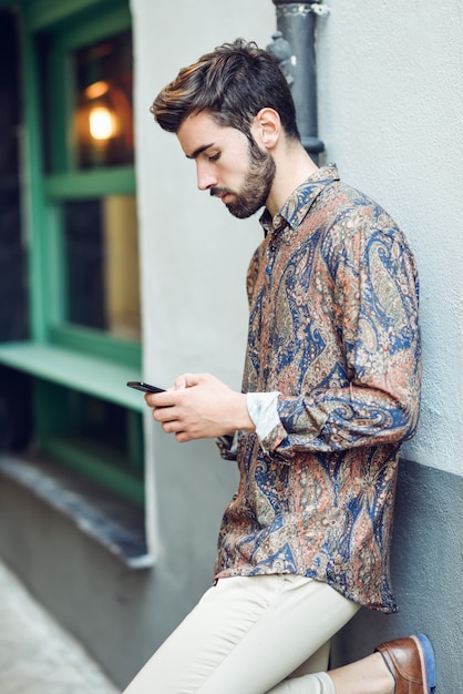 Jeune Homme Portant Des Vêtements Décontractés En Regardant Son Smartphone Dans La Rue.
