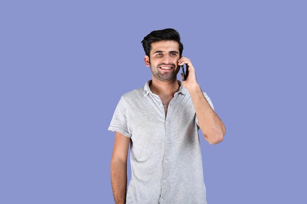 Jeune homme portant des vêtements d'été parlant au téléphone avec un visage souriant modèle pakistanais indien