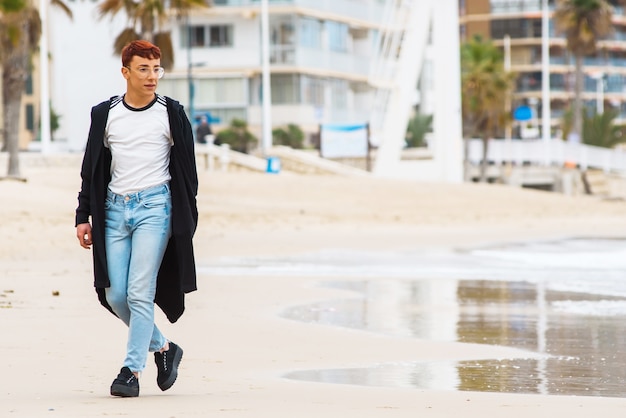 Jeune homme porté élégant marchant sur une plage