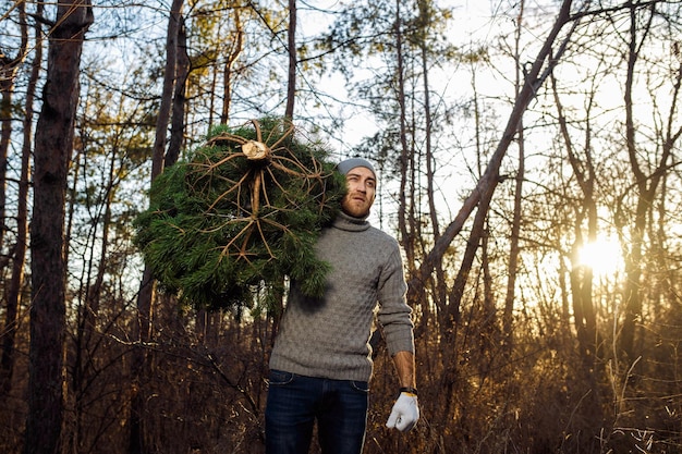 Photo un jeune homme porte un sapin de noël dans le bois des hommes barbus portent un sapin de noël à la maison.