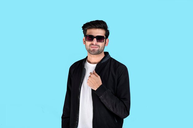 Jeune homme pose avant portant des vêtements d'hiver et des lunettes sur fond bleu modèle pakistanais indien