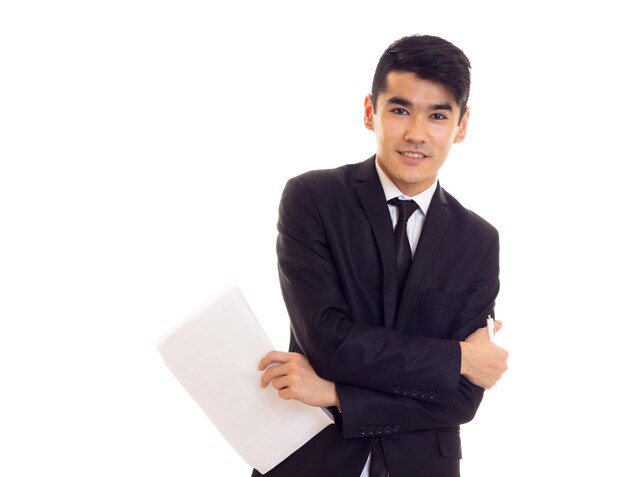 Jeune homme positif aux cheveux noirs en chemise blanche et costume noir avec cravate tenant des papiers