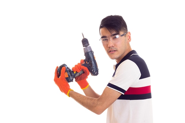 Jeune homme positif avec des gants orange et des lunettes de protection tenant un tournevis électrique gris