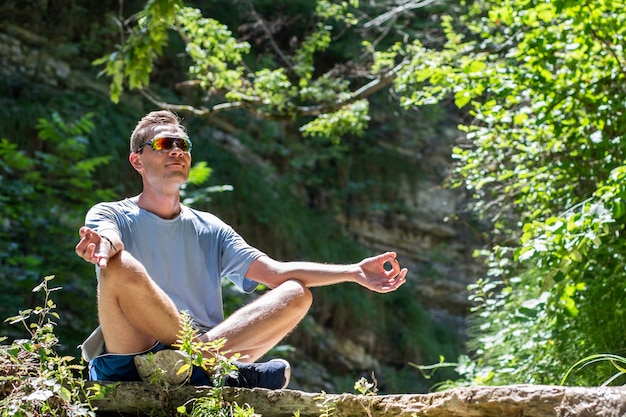 Un jeune homme en position du lotus est assis sur des pierres rocheuses dans le contexte d'une cascade et plus vert