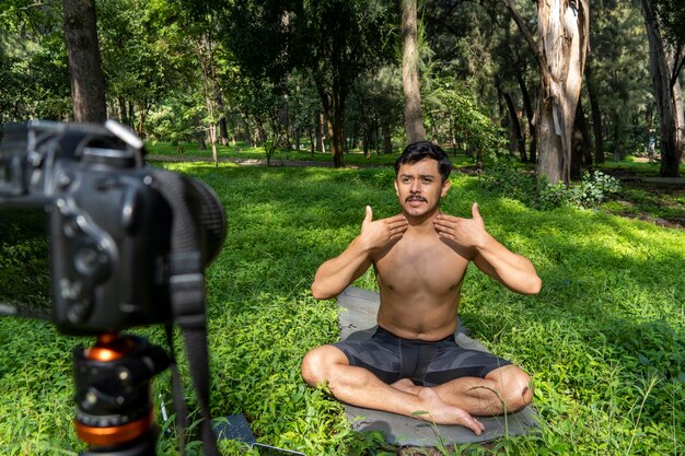 Jeune homme pratiquant le yoga asana équilibre méditant debout sur une jambe sur un tapis de sport sur l'herbe verte dans le parc à l'aide d'une tablette pour un cours en ligne