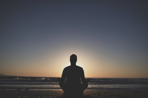Jeune homme pratique le yoga sur la plage au coucher du soleil.