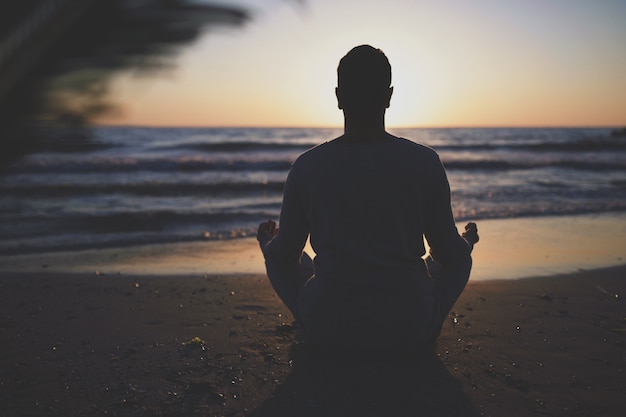 Jeune homme pratique le yoga sur la plage au coucher du soleil.