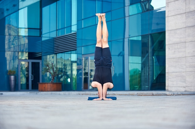 Jeune homme pratique le yoga poirier asana Sirsasana pose à l'extérieur