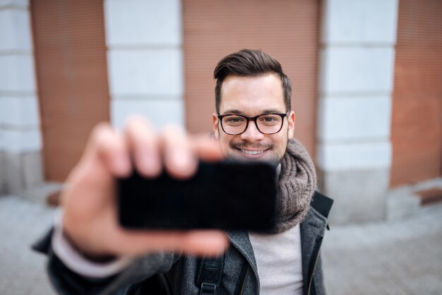 Jeune homme prenant selfie dans la ville, gros plan.