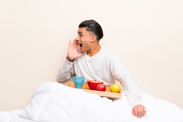 Jeune homme prenant son petit déjeuner au lit en criant avec la bouche grande ouverte