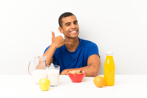 Jeune homme prenant son petit déjeuner dans une table en faisant un geste de téléphone