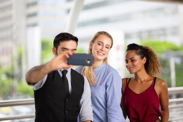 Un jeune homme prend un selfie avec son téléphone portable avec ses amis alors qu'il se tient sur un pont piétonnier.