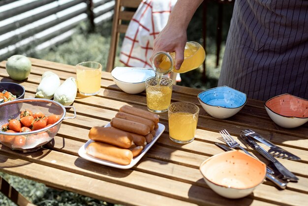 Jeune homme préparant une table pour un pique-nique, tenant une bouteille de limonade sous le soleil d'après-midi d'été. Barbecue de jardin